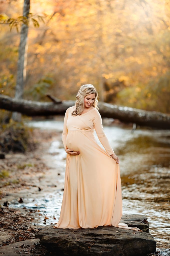 Beautiful mother poses in a flowy gown for maternity creek photos near Birmingham